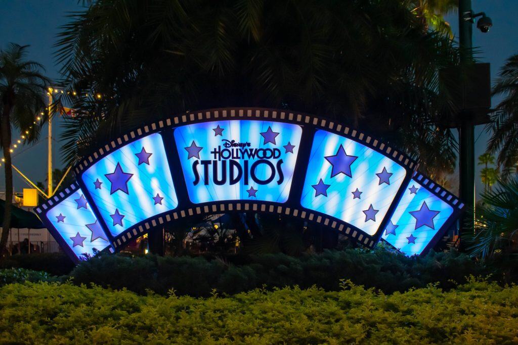 Hollywood Studios blue sign lit up with stars and shrubs at night